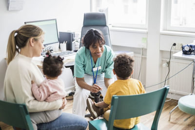 Smiling female doctor talking to boy while family in clinic