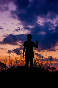 Rear view of woman standing on field against sky during sunset