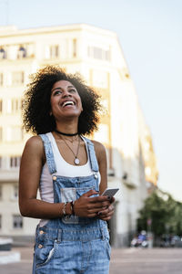 Smiling young woman using phone while standing in city