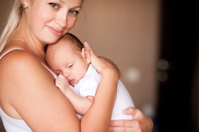 Smiling mother holding sleepy baby at home
