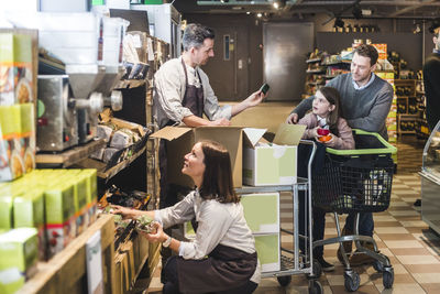 Salesman assisting customers while saleswoman arranging shelf in supermarket