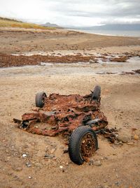 Rusty abandoned car on field against sky