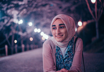 Portrait of smiling young woman in city at night