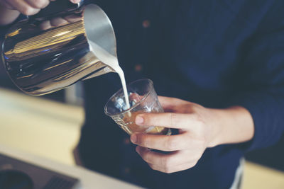 Midsection of man pouring milk in glass at cafe