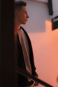 Side view of young man looking away against wall