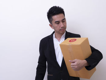 Young man holding camera while standing against white background