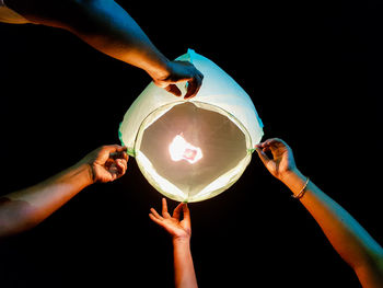 Cropped hands of people holding illuminated paper lantern against sky at n