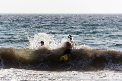 People playing, swimming in the waves in the island of patmos, greece in summer time