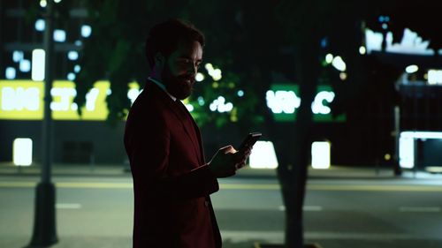 Side view of young woman standing in city at night