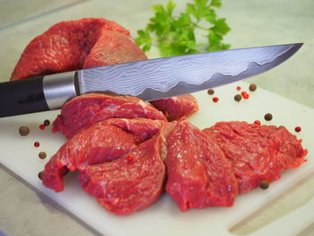 A damask steel knife with a pattern cuts red meat. chopped beef, slices, meat products