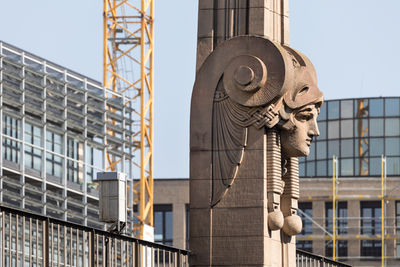 Yellow crane behind old concrete sculpture against modern office building and a construction site