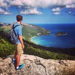 Man standing on cliff by sea against sky