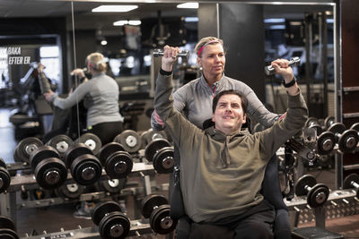 Man on wheelchair training in gym with personal trainer