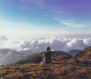 Rear view of woman sitting on mountain against sky