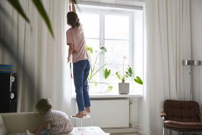 Full length of fashion designer measuring curtain while daughter playing on sofa at home