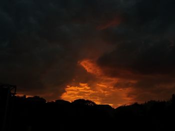 Silhouette trees against dramatic sky at sunset