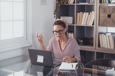 Woman looking away while sitting against shelf