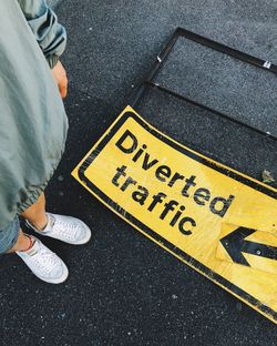 Low section of woman standing by information sign on road