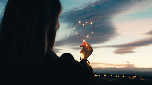 Rear view of woman with arms raised against sky during sunset