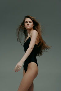 Portrait of young woman standing against gray background