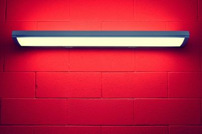 Low angle view of illuminated lighting equipment on red brick wall