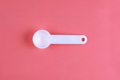 Close-up of white plastic spoon over coral background