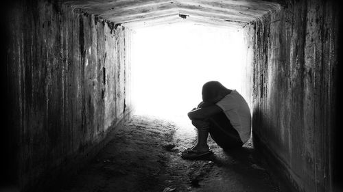 Side view of depressed boy sitting in tunnel against wall