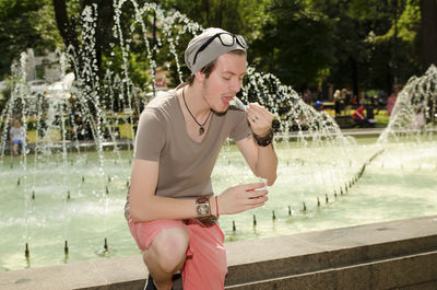 Young man eating ice cream by fountain in park