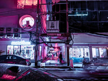 Illuminated street by buildings in city at night