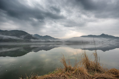 Scenic view of calm lake and mountains against cloudy sky