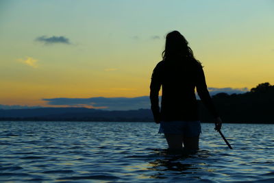 Rear view of silhouette man standing in sea against sunset sky