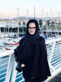 Portrait of smiling woman wearing warm clothing with harbor in background