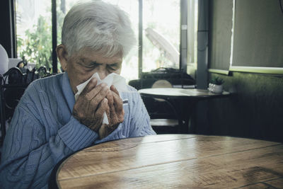 Old person coughing covering mouth with a tissue on a house interior. she has flu, allergy symptoms.