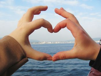 Cropped image of child making heart shape against sea