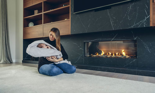 Mother with daughter sitting by fireplace at home