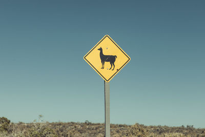 Road sign on field against clear sky