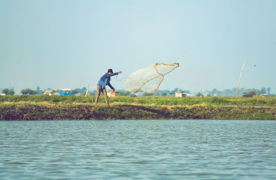 Rear view of a man is fishing in a pond against clear sky