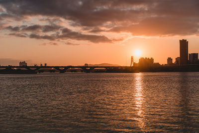 Sea by buildings against sky during sunset