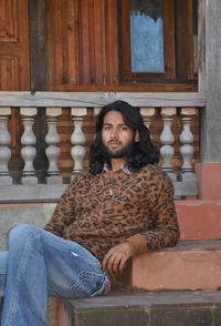 A handsome long haired indian young men looking at camera, posing with sitting on temple stairs