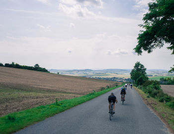 Rear view of people riding bicycle on road against sky