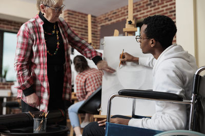 Man drawing on canvas while sitting on wheelchair