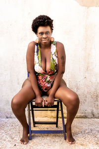 Portrait of smiling young woman sitting against wall