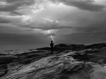 Rear view of man standing in front of sea against lightning