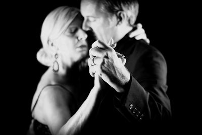 Close-up of couple holding hands against black background