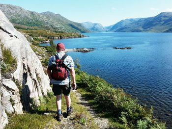 Rear view of hiker walking by river against clear sky