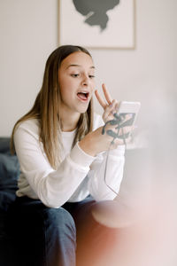 Teenage girl taking selfie through mobile phone while sitting at home