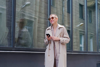 Smiling businesswoman using mobile while standing against building