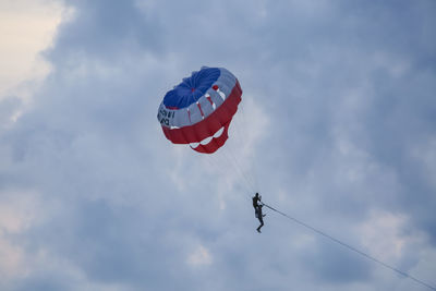 Low angle view of people paragliding against sky