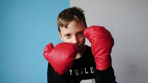 Portrait of confident boy with boxing gloves standing against wall