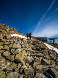 People on rock against blue sky